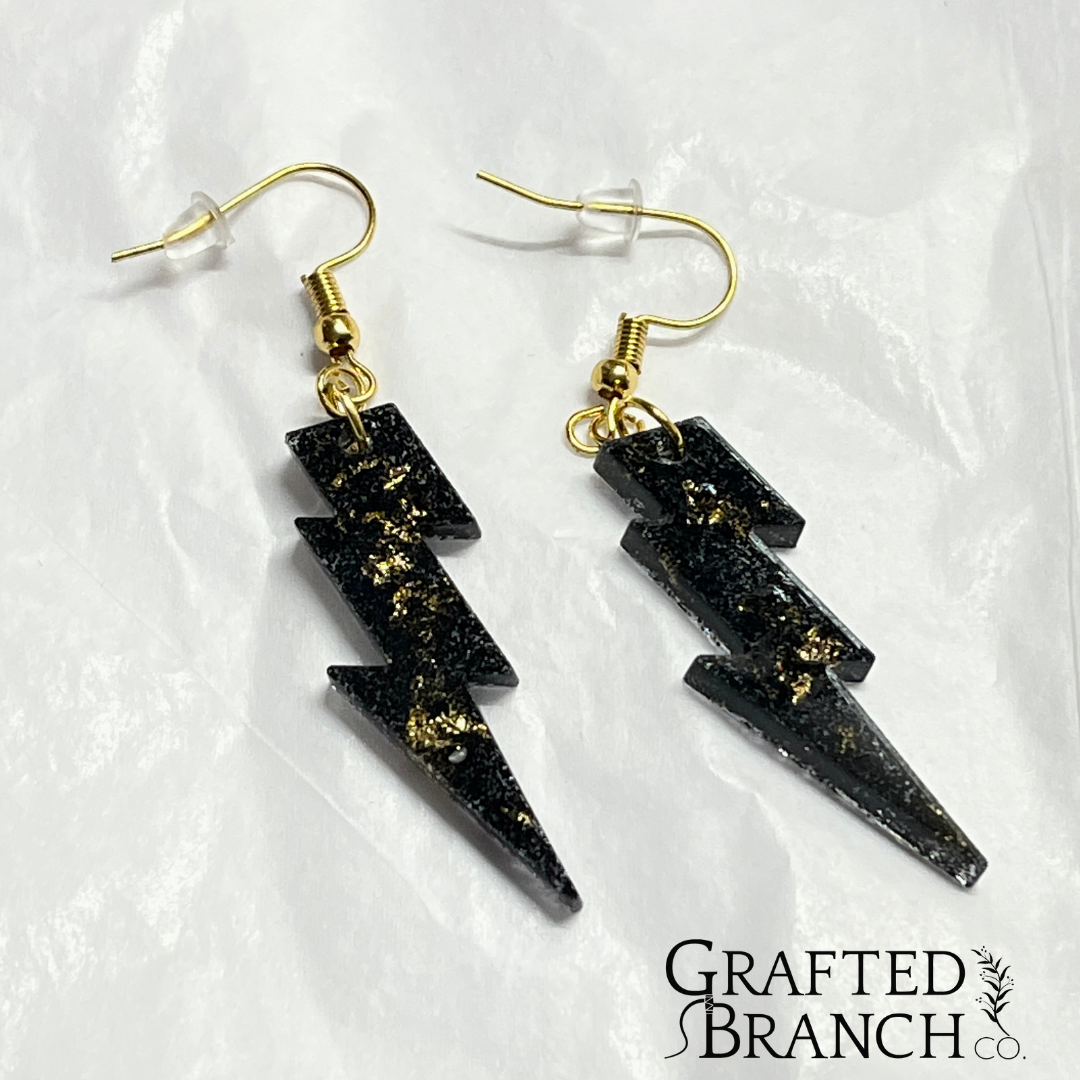 Earrings in the shape of a lightning bolt.  They are black with gold flecks and gold hooks.